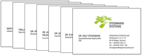 A stack of business cards for employees of Stegmann Systems. The top card belongs to Dr. Ralf Stegmann, CEO, and features the company's green logo, name, contact details, and address in Rodgau, Germany. The other cards, partially visible, display names and job titles of other team members.